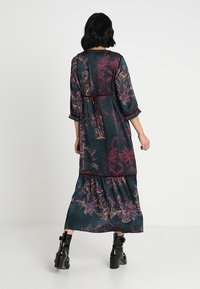 Blommig maxiklänning i mörkgrön med vinröda accenter. Har en lös passform, trekvartslånga ärmar och en skiktad nederdel. Mjuk textur, lättviktsmaterial.