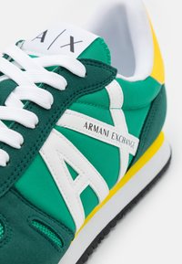 Sneakers verdes e cianos com detalhes brancos, apresentando o rótulo "ARMANI EXCHANGE", tecido texturizado e detalhes amarelos na sola.