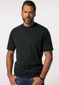 Sort kortærmet T-shirt med rund hals og synlig syning. Bæret sammen med blå denimjeans. Stoffet ser blødt og afslappet ud.