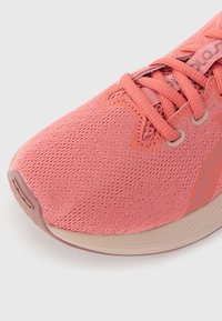 Chaussure de sport rose avec un upper en mesh texturé, présentant une pointe arrondie et un design à lacets. La semelle est beige avec des détails de relief subtils.