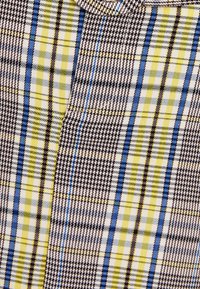 Tkanina s tkaným vzorem v kombinaci černé, žluté, modré a šedé barvy se čtvercovými vzory různých velikostí a detaily houndstooth.