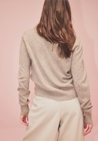 Beżowy sweter dzianinowy z okrągłym dekoltem i ściągaczami przy rękawach, zestawiony z jasnobeżowymi spodniami. Miękka tekstura, swobodny krój.