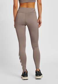 Strakke sportlegging in een gedempte taupekleur, met subtiele contrasterende stiksels en een geometrisch wit patroon langs het onderbeen.