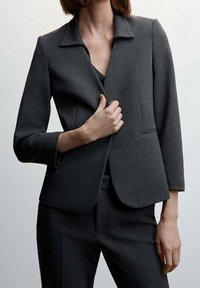 Blazer gris oscuro con cuello con muesca, cierre de un solo botón y solapas estrechas. El diseño estructurado y el corte ajustado mejoran la silueta general.
