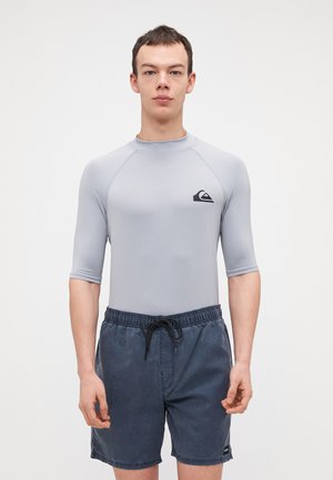 Grå kortermet rashguard med svart logo, sammen med mørkeblå svømmeshorts med elastisk liv og snøring.