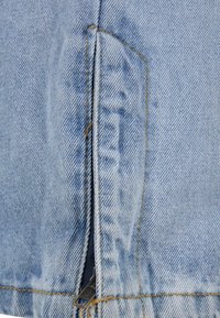 Tejido de mezclilla de color azul claro con un detalle de cremallera en el lateral, con costuras amarillas en contraste y una textura suave.