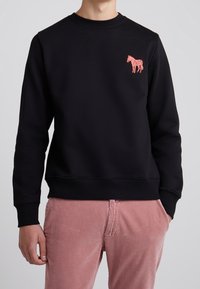 Svart sweatshirt i bomull med rund hals och ribbade muddar. Har en rosa broderad hästdetalj på vänster bröst.