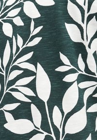 Λευκό μοτίβο φύλλου και κλαδιού σε σκούρο πράσινο υφασμάτινο φόντο με υφή.