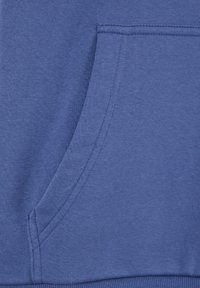 Il tessuto del sudore in cotone blu presenta una tasca a marsupio sul davanti. La trama è liscia con dettagli di cucitura visibili ai bordi.