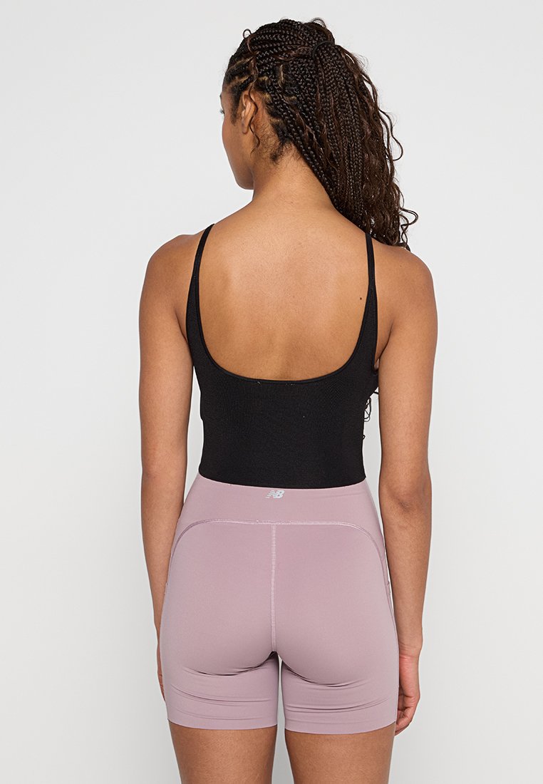 Bodysuit sin mangas negro combinado con pantalones cortos ajustados de un rosa claro, que cuentan con una cintura alta y un sutil branding en la cinturilla. Textura suave.