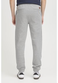 Grå sweatpants med elastisk talje, to baglommer og en subtil tekstur, parret med sort-hvide sneakers.