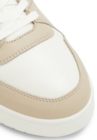 Béžové kožené sneakers s texturovaným bílým panelem, zdobené prošívanými detaily a bílými tkaničkami. Zaoblený tvar s plochou podešví.