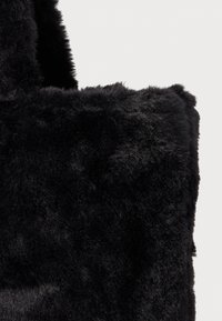 Zwarte faux fur tote bag met een pluizige textuur en stevige handvatten. Het ontwerp heeft een zachte, harige oppervlakte met een naadloze vierkante vorm.