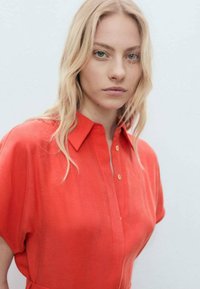 Abito camicia rosso a maniche corte con colletto e chiusura a bottoni, realizzato in tessuto leggero, con una superficie liscia e una vestibilità comoda.