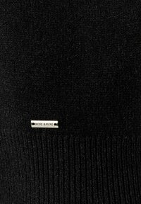 Schwarzer gestrickter Pullover mit geripptem Textur und einem silbernen Logo-Label, das "MORE & MORE" in den Stoff gestickt ist.