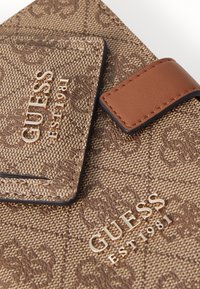Bruine gestructureerde portemonnee met het "GUESS" logo in goud, met een bruine leren sluiting. Opvallend reliëfontwerp en stiksels.