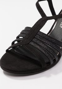 Czarne sandały z teksturowanego zamszu, z krzyżującymi się paskami i gładką podeszwą. Udekorowane subtelnym brokatem, podkreślającym design.