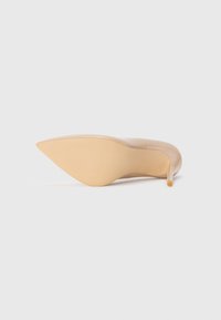 Stiletto cu toc subțire din lac nude, cu vârf ascuțit și textură netedă; talpa este bej, cu o ușoară curbură la toc.