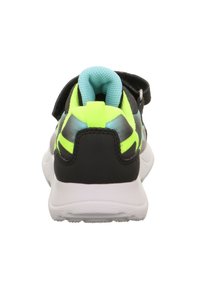 Black and neon yellow athletic shoes with a padded turquoise collar, hook-and-loop strap, and white rubber sole. Rear view showcases design accents.
