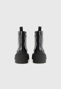 Bottes noires jusqu'aux chevilles au design épuré, avec une semelle épaisse et des fermetures éclair à l'arrière, sur un fond blanc uni.