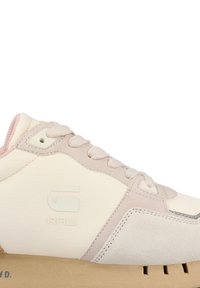 Baskets légères en crème et rose pâle, présentant un mélange de textures lisses et en daim, avec un logo en relief et une semelle en caoutchouc épaisse.