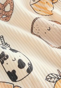 Egy krémszínű háttérrel rendelkező pamutszövet bordázott textúrával. Színes, játékos ételillusztrációk között szerepel egy fánk, fagylalt és egy tehén.