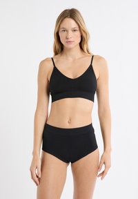 Bralette nero con spalline sottili e scollo a V abbinato a pantaloncini neri a vita alta. Tessuto strutturato con linee sottili.