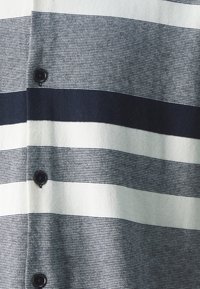 Detailní záběr na pruhovanou látku s černými knoflíky, která má střídavé široké a úzké horizontální černé a bílé pruhy.