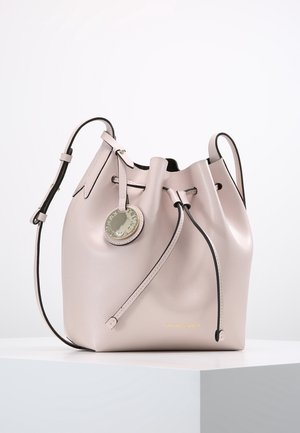 Bolso tipo cubo de color rosa claro con cierre de cordón, correa de hombro ajustable y colgante redondo de metal con logo, exhibido sobre una superficie blanca.