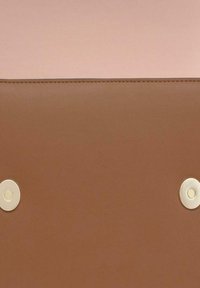 Producto de cuero marrón con una textura suave, que presenta una sección superior de color rosa claro y dos broches circulares de color claro.