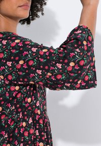 Robe fleurie avec un fond noir, ornée de fleurs roses et orange. Manches évasées détendues avec des détails froncés et un design fluide.