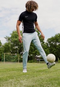 T-shirt de sport noir et blanc à manches courtes, pantalon bleu clair et chaussures de sport blanches, avec un ballon de soccer sur l'herbe verte.