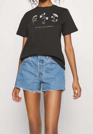 Sort bomulds-T-shirt med blomsterprint og teksten "no rain, no flowers" i hvid. Kombineret med lyseblå denimshorts med frynsede kanter.