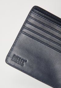 Navy leather wallet with multiple card slots, textured surface, and embossed "DIESEL" logo. Stitched edges add durability.