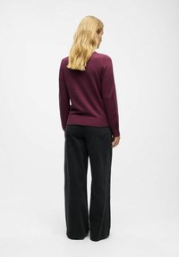 Marron striktrøje med ribbet kant, parret med højtaljede sorte vidde jeans, set fra bagsiden. Glat tekstur, afslappet design.