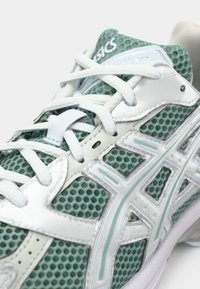 Leichter Laufschuh aus mintgrünem Mesh mit weißen synthetischen Überzügen, ausgestattet mit strukturierten Mustern und markanten Logo-Akzenten.