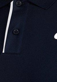 Marinblå pikétröja med två svarta knappar och ett vitt vertikalt rand längs knapplinjen på texturerad tyg.