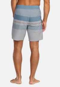 Pánske plavky v šedej farbe so vzorom horizontálnych modrých pruhov a jemnými červenými akcentmi, s viazaním v páse a detailmi bočných vreciek. Hladká textúra.
