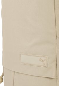 Beige sportdzseki, textúrált anyaggal, rejtett cipzárral és Puma logóval az oldalon. Minimalista dizájn, letisztult vonalakkal.