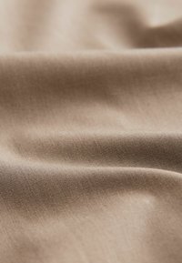 Tissu beige avec une surface lisse et légèrement texturée, présentant de légères rides et un doux éclat, indiquant un matériau léger.