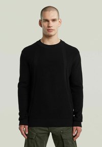 Maglione nero a maglia con una texture a coste, scollo rotondo e maniche lunghe. Abbinato a pantaloni cargo oliva per un contrasto.