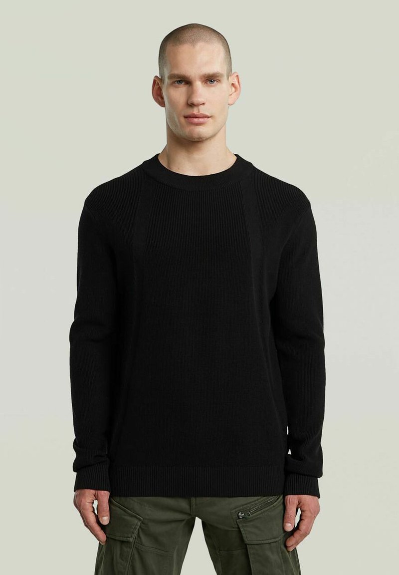 Maglione nero a maglia con una texture a coste, scollo rotondo e maniche lunghe. Abbinato a pantaloni cargo oliva per un contrasto.