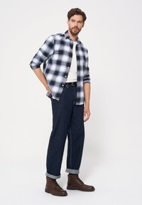 Koszula w kratę w czarno-białym kolorze, noszona na bia�łej koszulce; ciemnoniebieskie dżinsy z podwiniętymi nogawkami; brązowe skórzane botki do kostki.