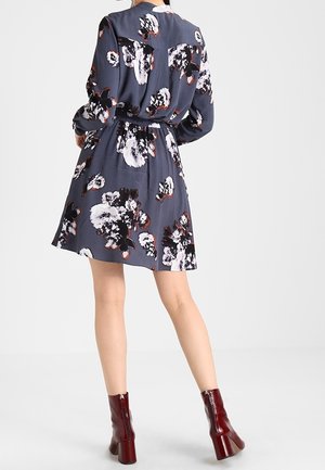Robe à motifs floraux en tissu bleu foncé avec une taille cintrée, des manches longues et une jupe évasée. Associée à des bottines bordeaux.