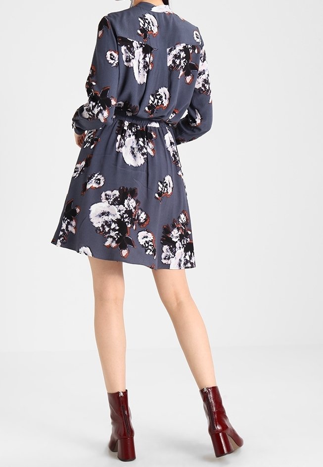 Robe à motifs floraux en tissu bleu foncé avec une taille cintrée, des manches longues et une jupe évasée. Associée à des bottines bordeaux.