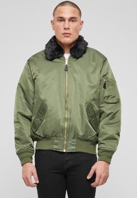 Alyvuogių žalios spalvos bombonešio striukė su dirbtiniais kailio apykakle, ribiniu rankogaliu ir apačia, dvi šoninės kišenės ir užtrauktuku užsegama rankovės kišenė. Lygus, blizgus audinys.