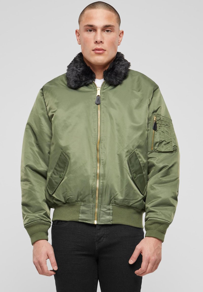 Alyvuogių žalios spalvos bombonešio striukė su dirbtiniais kailio apykakle, ribiniu rankogaliu ir apačia, dvi šoninės kišenės ir užtrauktuku užsegama rankovės kišenė. Lygus, blizgus audinys.