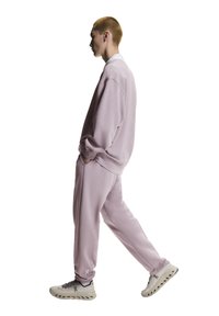 Hellviolettes Sweatshirt und passende Jogginghose aus weichem Stoff. Mit lockerem Schnitt, gerippten Bündchen und Logodetail an der Hose. Kombiniert mit hellen Sneakern.