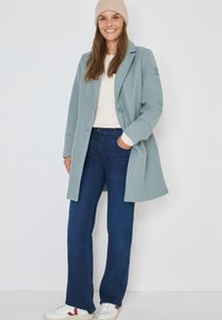 Lichtblauwe jas met een op maat gemaakt ontwerp, notch revers en een enkele knoopsluiting. Gecombineerd met donkerblauwe jeans en witte sneakers.