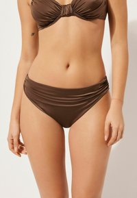 Ensemble de bikini brun comprenant un haut bralette froncé et un bas taille haute en tissu lisse et brillant. Chaque pièce a une coupe classique.